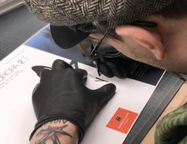 Tobi Tietchen signiert 100 MS Europa 2 Kataloge mit der Tattoo-Nadel